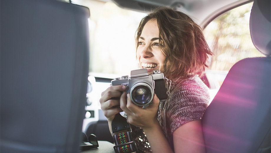 uśmiechnięta kobieta siedzi w samochodzie na fotelu z aparatem fotograficznym lustrzanką
